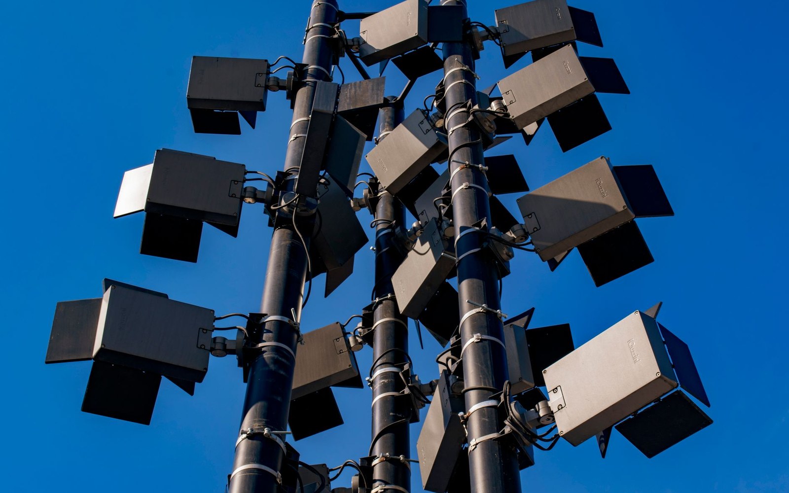 A stadium floodlight bank photographed from directly below, lights on, sky dark behind them