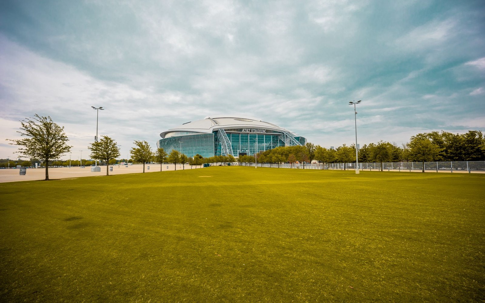 AT&T Stadium's arched glass facade viewed across an open grass field