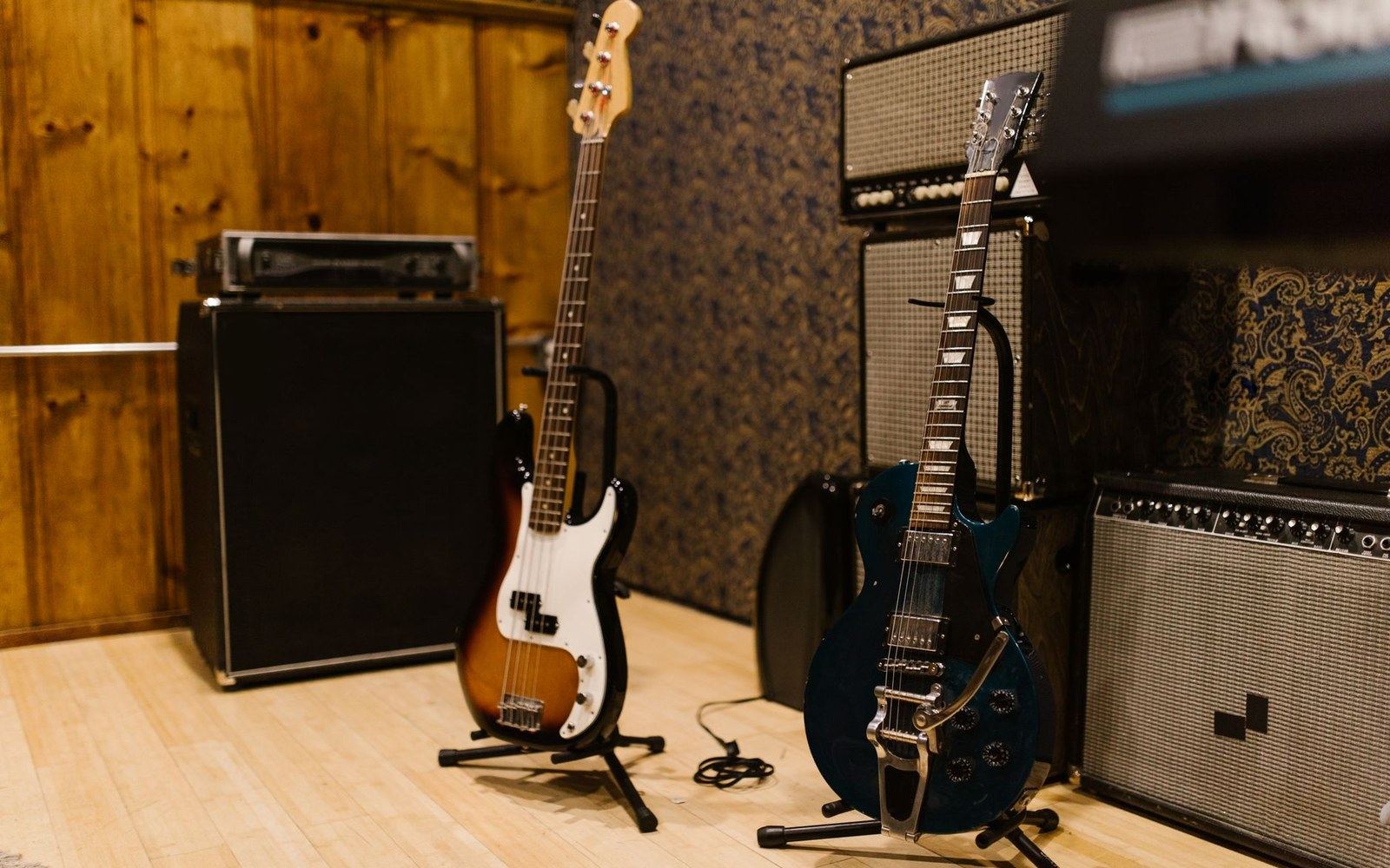 Bass and electric guitars on stands surrounded by amplifiers in a studio