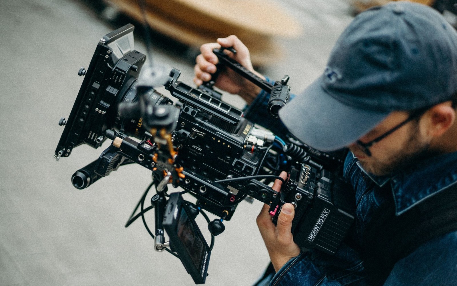 A man wearing a baseball cap operates a professional cinema camera rig outdoors