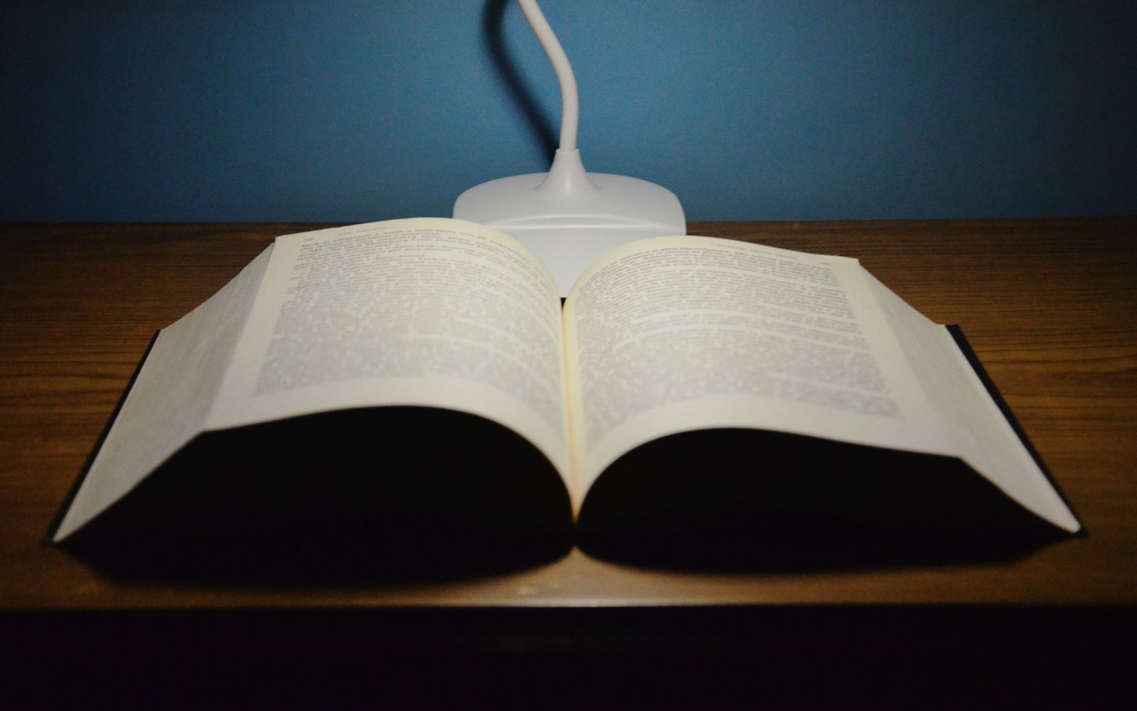 An open thick book on a wooden table under a small desk lamp