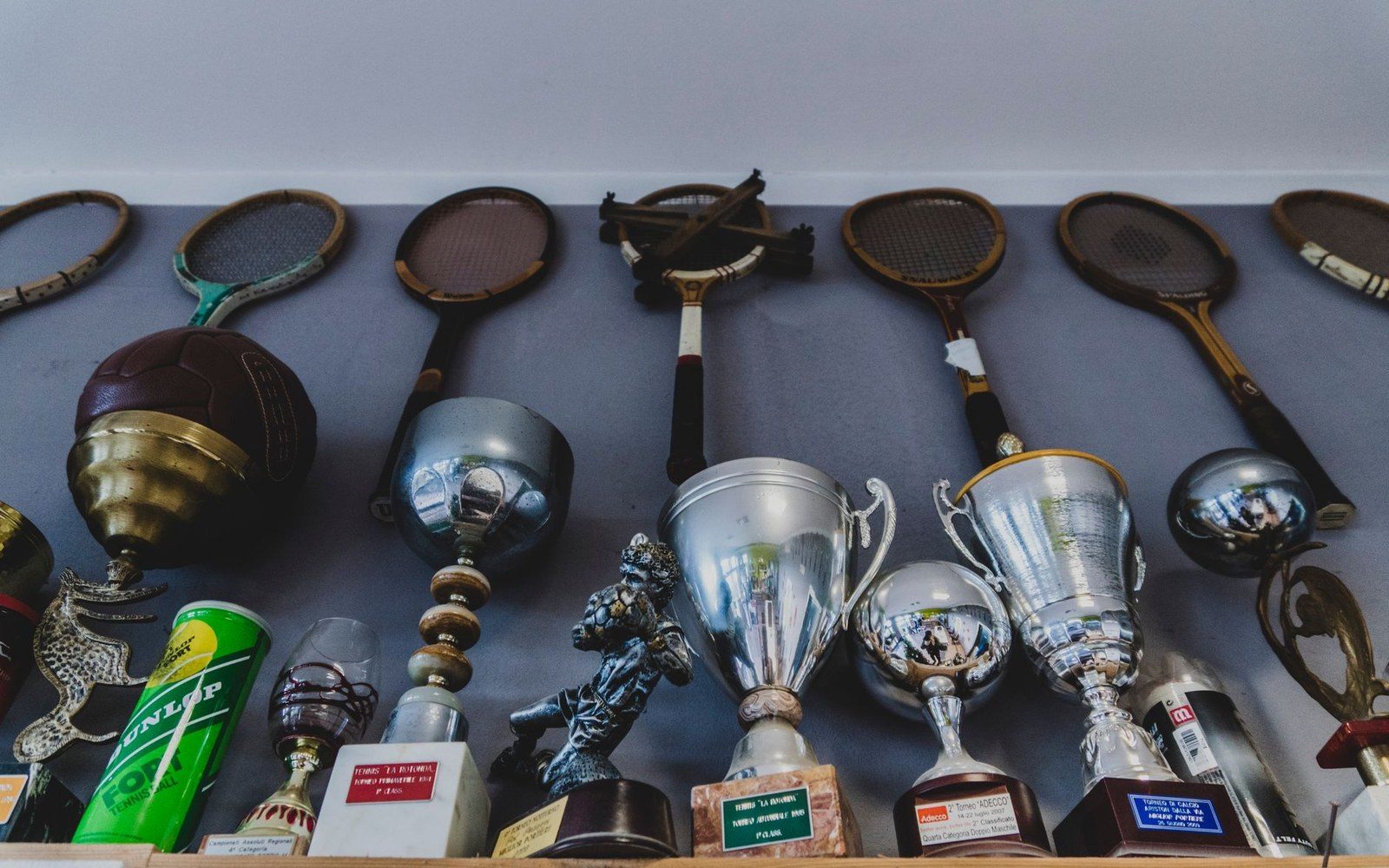 Vintage tennis rackets mounted above a shelf of silver trophies and cups